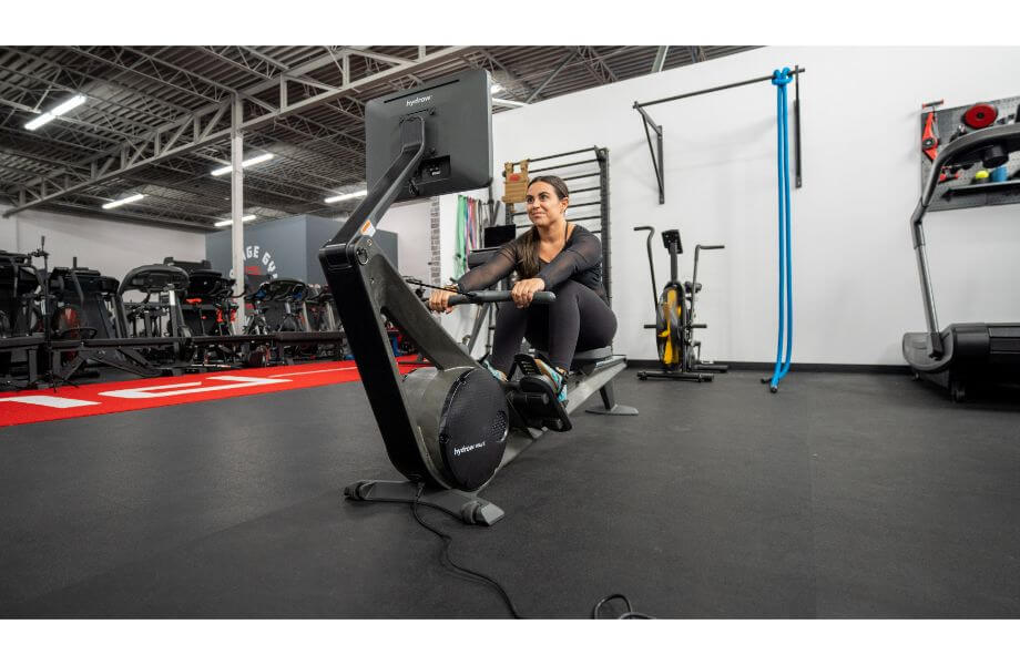 A woman in a gym setting using a Hydrow Wave rowing machine